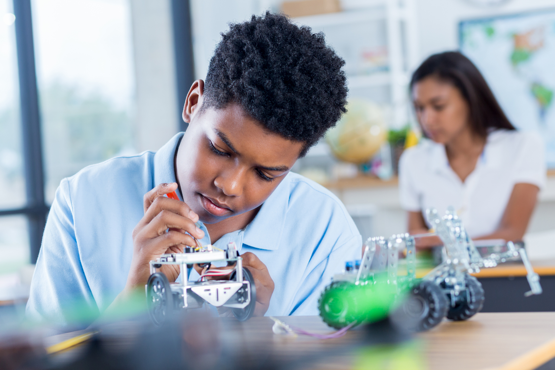 A teen focused on soldering a robot car's circuit board at a workbench